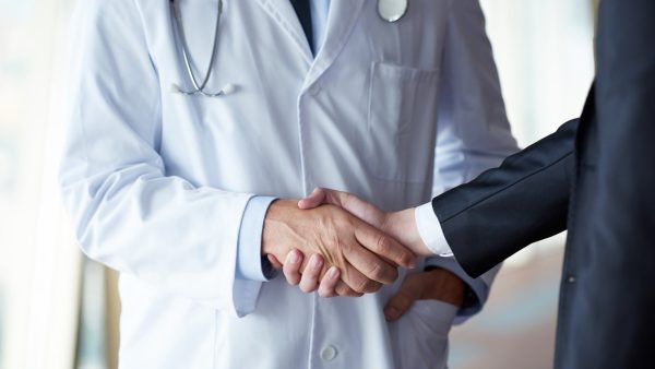 Un médico y un representante médico se saludan con un apretón de manos en un consultorio.