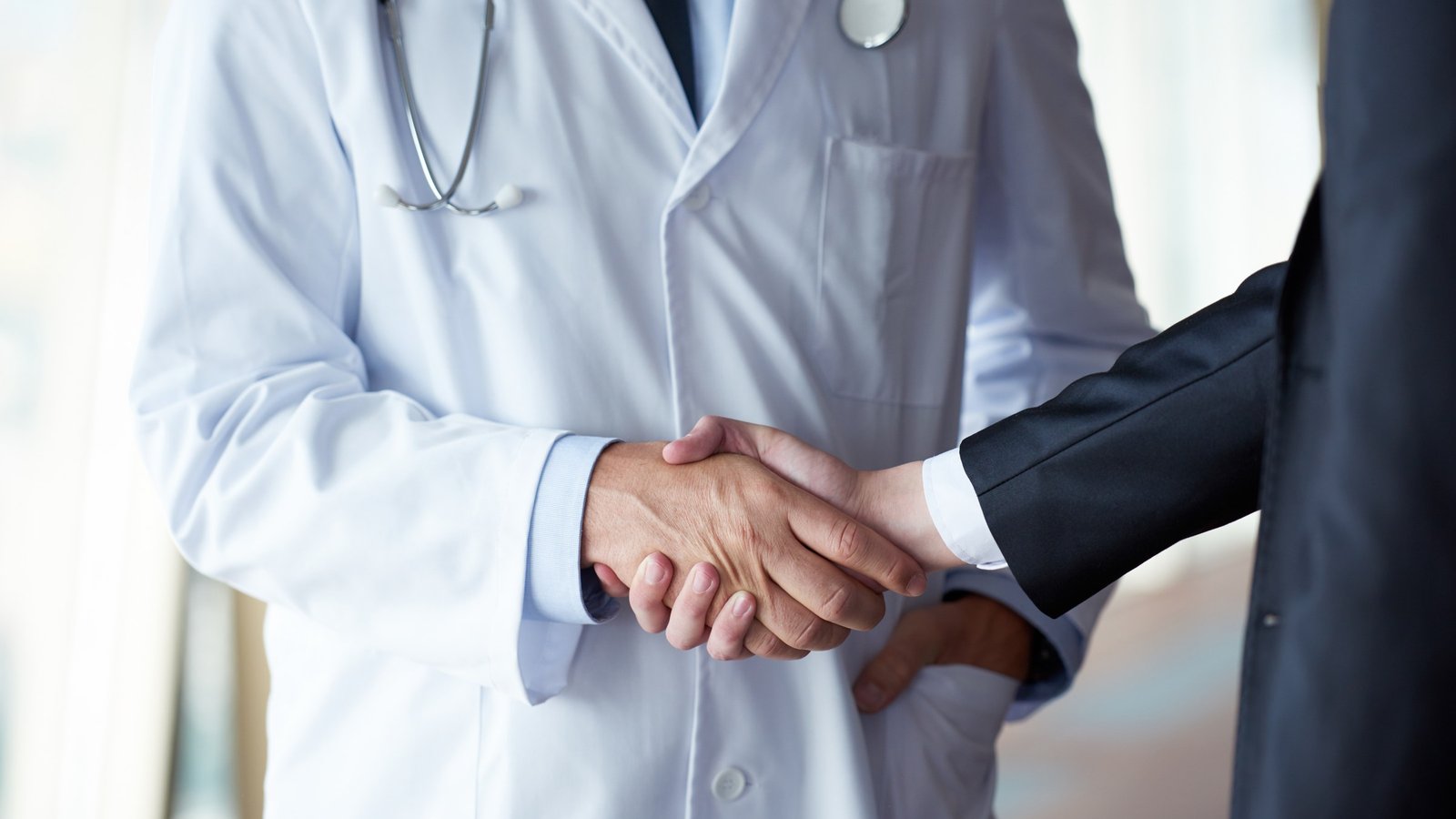Un médico y un representante médico se saludan con un apretón de manos en un consultorio.